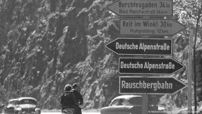 Foto antiga mostra placas de orientação para motoristas sobre a rota dos Alpes