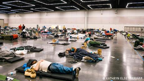 People lying on makeshift beds in a gym 