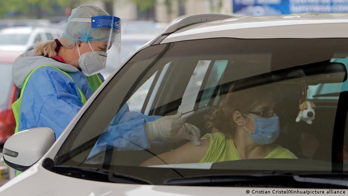 A nurse vaccinating a masked woman in a car