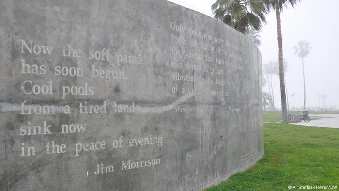 A memorial in Venice Beach for Jim Morrison, gray stone wall on the grass, palm trees in the background