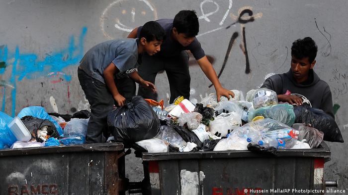 Two boys and an adult search through garbage containers for valuables and for metal cans that can be resold, in Beirut, Lebanon, on June 17, 2021