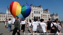 08.07.2021, Ungarn, Budapest: Aktivisten gehen an einem großen regenbogenfarbenen Herz vorbei, das vor dem Parlamentsgebäude aufgestellt wurde. Die Aktivisten protestieren gegen das kürzlich verabschiedete Gesetz, das ihrer Meinung nach LGBT-Menschen diskriminiert und ausgrenzt. Foto: Laszlo Balogh/AP/dpa +++ dpa-Bildfunk +++