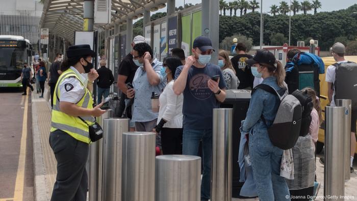 Menschen mit Maske stehen an einem Bus-Terminal