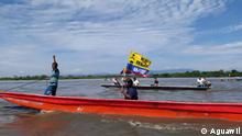 Dos hombres navegan el río Magdalena en una canoa motorizada, uno de ellos sentado en la mitad del vehículo, ondea una bandera de “No al Fracking”.
Credits: Aguawil
