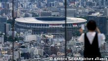 A person wearing a protective mask takes a picture from an observation deck as National Stadium, where the opening ceremony of the Tokyo 2020 Olympics will be held in less than two weeks is seen in the background Saturday, July 10, 2021, in Tokyo. (AP Photo/Kiichiro Sato)