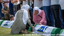 Women react as mourners prepare for the funeral of newly identified victims at the memorial cemetery in Potocari near Srebrenica, Bosnia, Sunday, July 11, 2021. Bosnia is marking the 26th anniversary of the Srebrenica massacre, the only episode of its 1992-95 fratricidal war that has been declared a genocide by international and national courts. The brutal execution of more than 8,000 Muslim Bosniaks by Bosnian Serb troops is being commemorated by a series of events Sunday. (AP Photo/Darko Bandic)