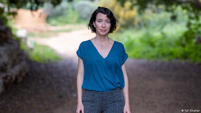 Author Ayelet Gundar-Goshen stands on a shaded country road 