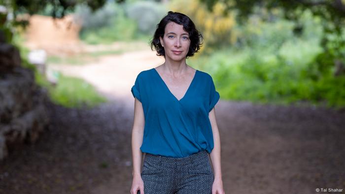 Author Ayelet Gundar-Goshen stands on a shaded country road 