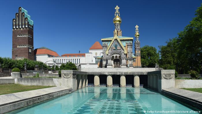 Foto mostra, à esquerda, uma torre. Há uma espécie de piscina e uma construção que se assemelha a uma capela. 