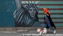 08.05.2018, Iran, Teheran: Eine Frau geht mit ihrem Hund vor einem USA-kritischen Wandbild der Freiheitsstatue mit Totenkopf am Gebäude der ehemaligen amerikanischen Botschaft in Teheran vorbei. US-Präsident Trump hat angekündigt am 08.05.2018 seine Entscheidung zum Atomdeal mit dem Iran zu verkünden. Foto: Vahid Salemi/AP/dpa +++ dpa-Bildfunk +++