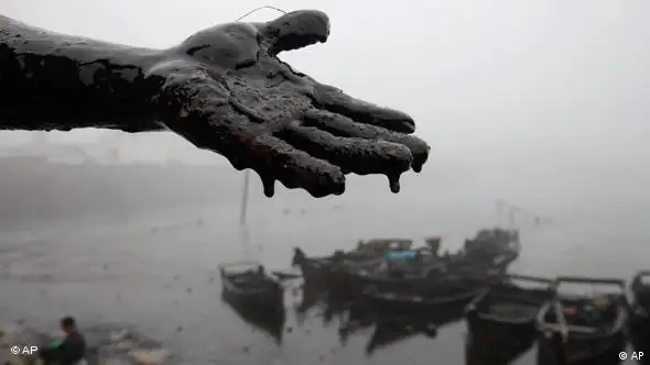 Un habitante de la bahía de Weitang en China muestra su mano cubierta de petróleo. Una explosión había causado el derrame más grande del país, en julio de 2010.