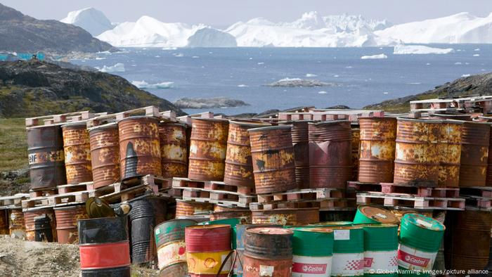 Waste oil barrels on the tundra outside Illulissat in Greenland with icebergs behind from the Sermeq Kujullaq or Illulissat Ice fjord.