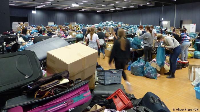 A large room filled with people, boxes and bags