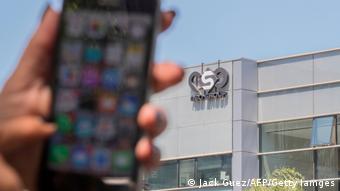 Foto simbólica de una mano con un celular frente a la sede de NSO Group.