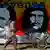 Ein Arbeiter geht mit einer Schubkarre an einem Graffiti vorbei. Darauf abgebildet sind Kubas Unabhängigkeitskämpfer Jose Marti, Kubas Revolutionsheld Ernesto "Che" Guevara und Chiles ehemaliger Präsident Salvador Allende (Foto: AP Photo/Esteban Felix)
