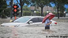 TOPSHOT - This photo taken on July 20, 2021 shows a man wading past a submerged car along a flooded street following heavy rains in Zhengzhou in China's central Henan province. - - China OUT (Photo by STR / AFP) / China OUT (Photo by STR/AFP via Getty Images)