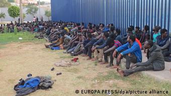 مجموعة من المهاجرين الأفارقة يجلسون أمام مركز إيواء في مليلية الاسبانية