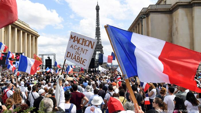 Foto mostra muitas pessoas, com a torre Eifel ao fundo. Algumas portam bandeiras da França. 