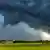 A massive, dark storm cloud moves over a green field in Bavaria