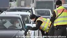 Masked border police officer leans into the window of a car where a masked woman sits