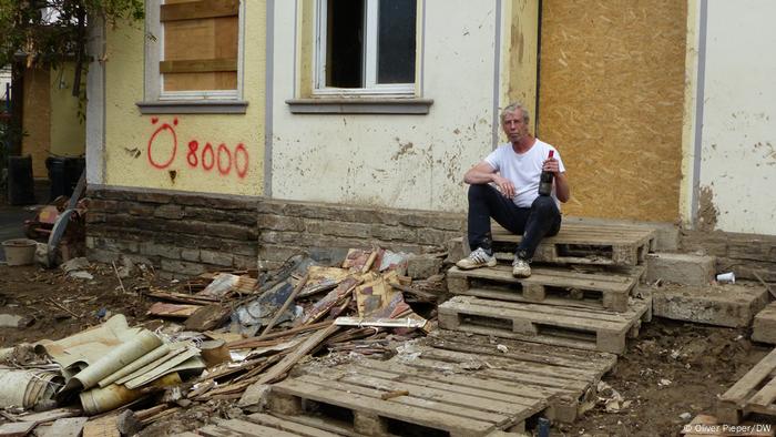 Bernd Schumacher hält seine Flasche Rotwein und sitzt auf den Stufen seines zerstörten Hauses