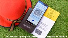 Ein Sonnenhut mit einem Reisepass, Impfbuch, digitalem Impfzertifikat und digitalem Impfzertifikat auf einem Mobiltelefon. (Themenbild, Symbolbild, Model Release, Geänderte QR-Code)