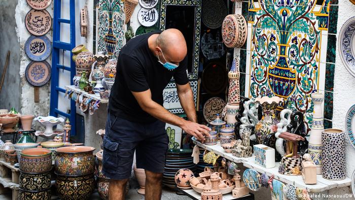 A man organises colorful ceramics in a Tunisian market. 
