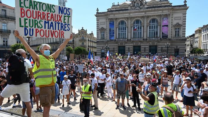Protester in a yellow vest holds up a placard in front of a crowd of people demonstrating