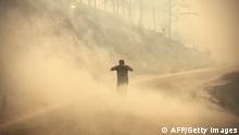 TOPSHOT - A pedestrian walks through the smoke as a massive wildfire which engulfed a Mediterranean resort region on Turkey's southern coast near the town of Manavgat, on July 30, 2021. - At least three people were reported dead on July 29, 2021 and more than 100 injured as firefighters battled blazes engulfing a Mediterranean resort region on Turkey's southern coast. Officials also launched an investigation into suspicions that the fires that broke out Wednesday in four locations to the east of the tourist hotspot Antalya were the result of arson. (Photo by - / AFP) (Photo by -/AFP via Getty Images)