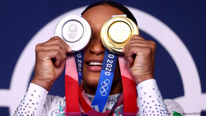 Rebeca segura a medalha de prata em frente a um olho e a de outro em frente a outro. 