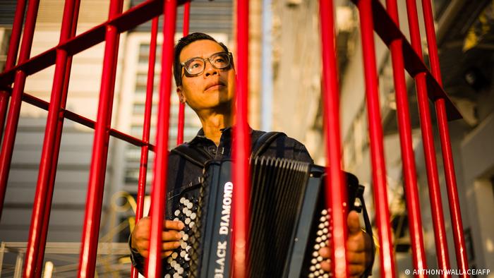 Man with glasses playing an accordion inside a red cage