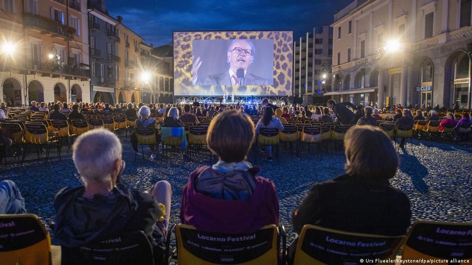 Audience members watch Festival President Luciano Giudici onscreen at the Piazza Grande