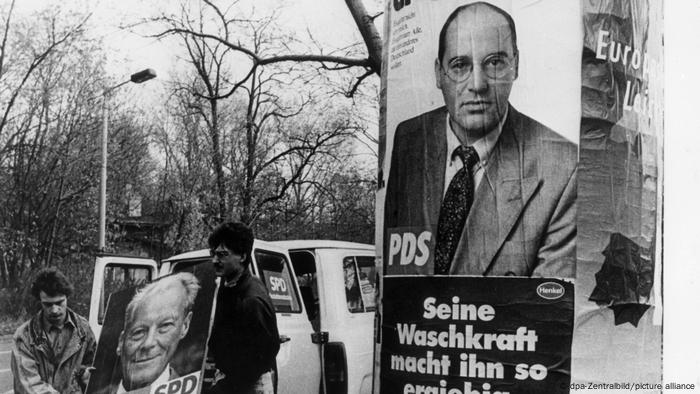 Unter einem Wahlplakat der PDS für die ersten gesamtdeutschen Bundestagswahlen am 02.12.1990 hängt ein Plakat für Waschmittel mit dem Slogan Seine Waschkraft macht ihn so ergiebig.
