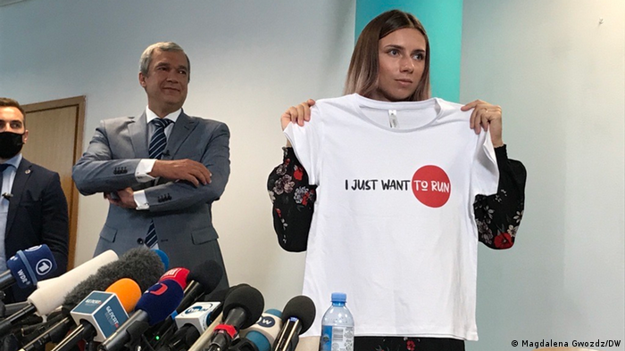 Tsimanouskaya holds up a white t-shirt with the words 'I just want to run' printed on it