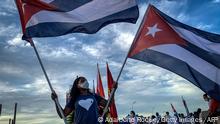 TOPSHOT - A woman holds Cuban flags during a caravan organized by the Union of Young Communists for love, peace and solidarity, along Havana's waterfront on August 5, 2021. (Photo by ADALBERTO ROQUE / AFP) (Photo by ADALBERTO ROQUE/AFP via Getty Images)