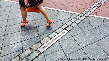 A woman steps over markings on the ground showing the former path of the Berlin Wall