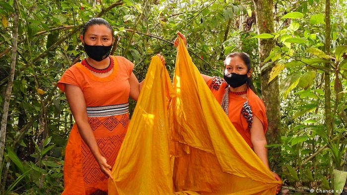 Dos mujeres yanesha sostienen telas anaranjadas.