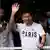 Lionel Messi waves while wearing a shirt that reads "Paris" 
