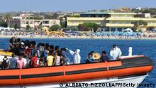 Migrants from Tunisia and Lybia are examined as they arrive onboard of an Italian Guardia Costiera (Coast Guard) boat in the Italian Pelagie Island of Lampedusa, while a beach with tourists is seen in the background, on August 1, 2020. (Photo by Alberto PIZZOLI / AFP) (Photo by ALBERTO PIZZOLI/AFP via Getty Images)