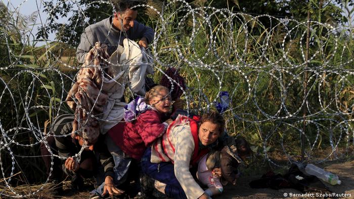 Семья беженцев с детьми пытается проникнуть через заграждение из колючей проволоки на границе Сербии с Венгрией