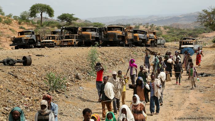 Villagers return from a market to Yechila town in south central Tigray walking past scores of burned vehicles, in Tigray, Ethiopia, July 10, 2021