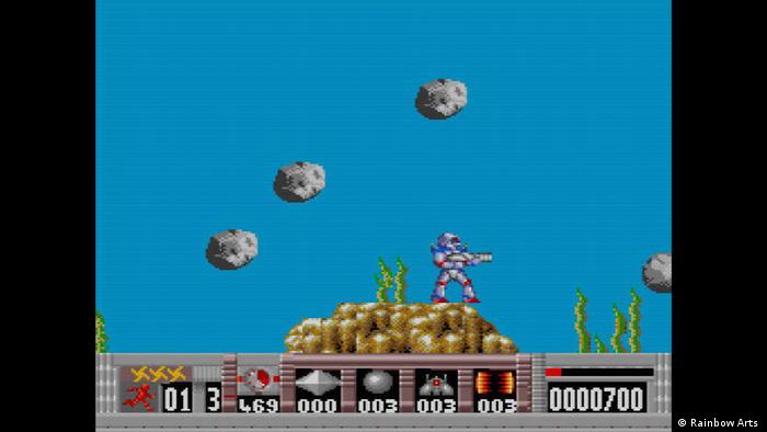 Screenshot from Turrican shows figure wil a weapon standing on a pile of sth golden and aiming and stones flying around.