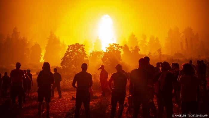 People gather in an open field and wait to support firefighters during a wildfire next to the village of Kamatriades, near Istiaia, northern Evia (Euboea) island on August 9, 2021