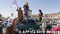 Taliban fighters stand over a damaged police vehicle along the roadside in Kandahar on August 13, 2021. (Photo by - / AFP) (Photo by -/AFP via Getty Images)