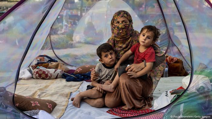 A veiled woman sits in a refugee tent with her two children.