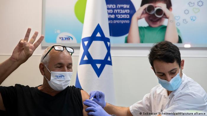 A man gets his third COVID shot next to an Israeli flag