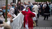 An Iranian woman wearing a protective face mask looks on as people line-up out of a sport hall while waiting to receive a dose of the China's Sinopharm new coronavirus disease (COVID-19) vaccine in central Tehran on July 19, 2021. (Photo by Morteza Nikoubazl/NurPhoto)