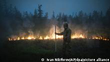 22.07.2021, Russland, Gorny: Ein Freiwilliger geht an brennenden Gras in der Nähe des Feuers westlich der Stadt Jakutsk vorbei. In weiten Teilen Russlands kam es aufgrund von ungewöhnlich hohen Temperaturen und der Vernachlässigung von Brandschutzvorschriften zu Waldbränden, wobei die Region Sacha-Jakutien im Nordosten Sibiriens am stärksten betroffen ist. Foto: Ivan Nikiforov/AP/dpa +++ dpa-Bildfunk +++