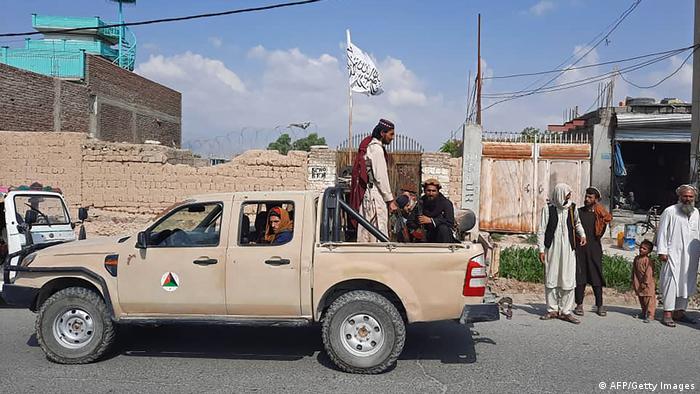 Taliban fighters drive an Afghan National Army vehicle through the streets as villagers look on