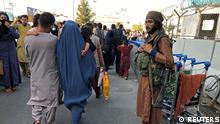 A member of Taliban stands guard as people walk at the entrance gate of Hamid Karzai International Airport in Kabul, Afghanistan, August 16, 2021.REUTERS/Stringer